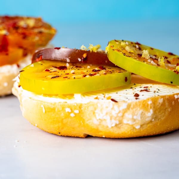 A Beverly Hills Bagel with cream cheese, green and brown tomato slices, and spices.