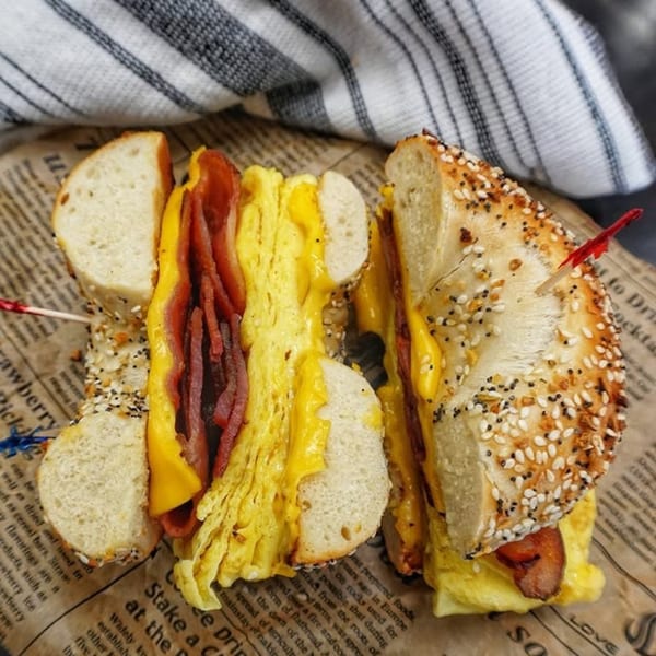 Beverly Hills Bagel's everything bagel sandwich with bacon, egg, and cheese, served on newspaper.