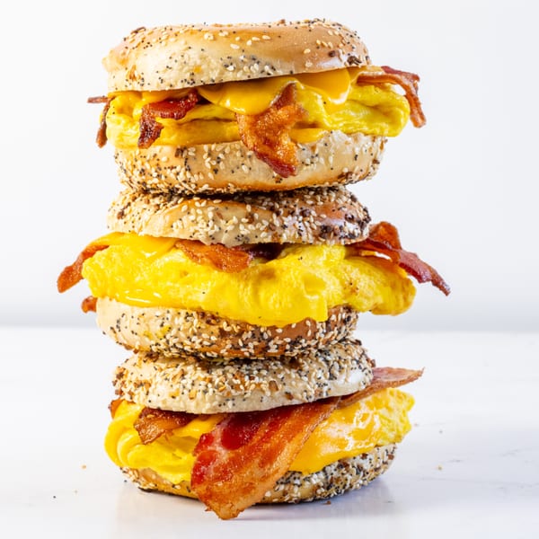 A tall stack of three everything bagels with scrambled eggs, melted cheese, and crispy bacon.
