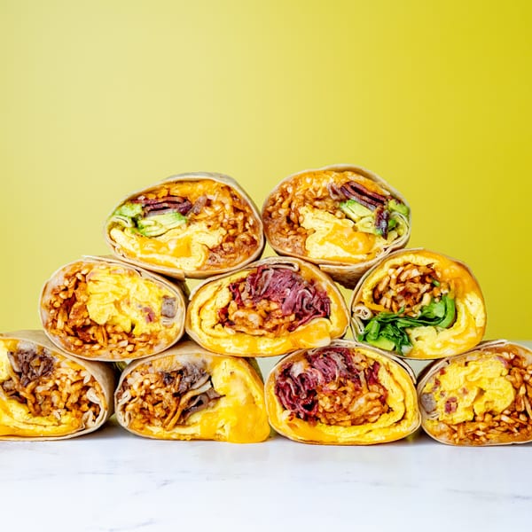A pyramid stack of various breakfast burritos, cut in half to show fillings, against a yellow background.